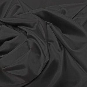 May include: A close-up of a smooth, black fabric with a soft, flowing texture. The fabric is draped and folded, creating a sense of movement and depth.