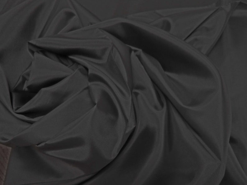 May include: A close-up of a smooth, black fabric with a soft, flowing texture. The fabric is draped and folded, creating a sense of movement and depth.