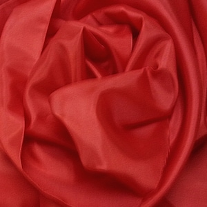 May include: Close-up of a red fabric with soft, flowing folds. The fabric is smooth and silky, creating a luxurious and elegant look.