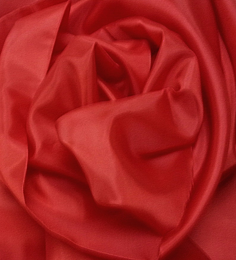 May include: Close-up of a red fabric with soft, flowing folds. The fabric is smooth and silky, creating a luxurious and elegant look.