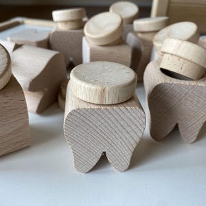 Könnte beinhalten: Ein Satz Holzspielzeugzähne mit Deckeln. Die Zähne sind aus Naturholz gefertigt und haben eine glatte Oberfläche. Die Deckel sind ebenfalls aus Holz und haben eine abgerundete Form.