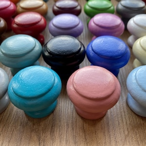 Könnte beinhalten: Sortiment an runden, bunten Schrankknöpfen in verschiedenen Farben, darunter Blau, Grün, Rosa, Rot und Weiß.