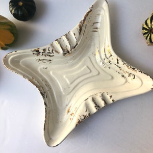 May include: White ceramic ashtray with a star shape and gold accents. The ashtray has a worn, vintage look.