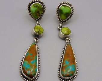 May include: A pair of dangle earrings with turquoise stones set in silver. The earrings feature a teardrop-shaped stone with a green and brown color pattern, a smaller round green stone, and a teardrop-shaped stone with a green and brown color pattern.