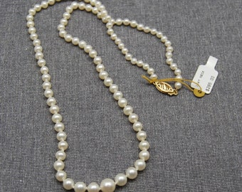 May include: A white pearl necklace with a gold clasp. The necklace is on a gray fabric background and has a price tag that says "$285.00".