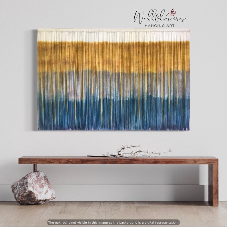 A boho fabric wall hanging with a colorful geometric print on a wooden dowel, decorating a living room wall.
