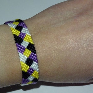 Op de afbeelding: Een vriendschapsarmband met een chevron-patroon in de kleuren paars, geel en zwart.