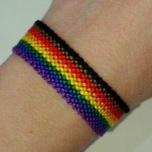 Peut inclure: Un bracelet d'amitié arc-en-ciel avec des rayures noires, violettes, bleues, vertes, jaunes, oranges et rouges.