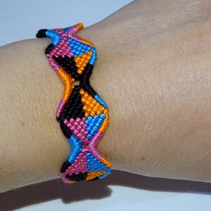 Op de afbeelding: Een kleurrijk vriendschapsarmband met een geometrisch patroon in roze, blauw, oranje en zwart.