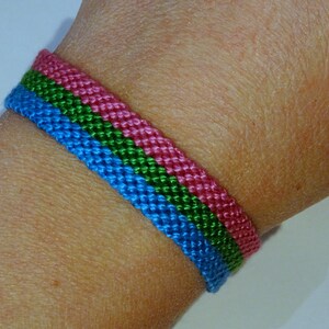 Pode incluir: Um bracelete de amizade azul, verde e rosa feito com corda trançada.