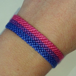 Op de afbeelding: Een blauwe, paarse en roze vriendschapsarmband geweven met een eenvoudig patroon.