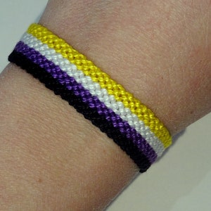 Pode incluir: Um bracelete de amizade com listras amarelas, brancas, roxas e pretas.