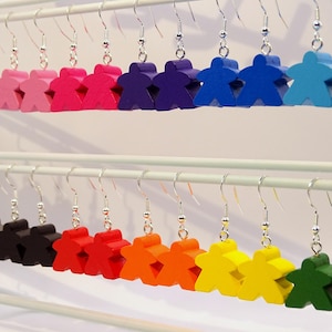 Op de afbeelding: Een display van kleurrijke houten spelstuk oorbellen. De oorbellen zijn in verschillende kleuren, waaronder wit, roze, rood, paars, blauw, grijs, zwart, oranje, geel en groen. Elke oorbel heeft een zilveren haak.