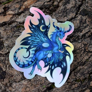 May include: A blue and black iridescent sticker of a dragon with butterfly wings. The dragon has a long tail and a crescent moon on its wings.
