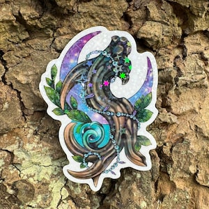 Puede incluir: Una pegatina holográfica con una luna creciente, un diseño arremolinado turquesa y azul, y una forma estilizada de árbol. El diseño incluye hojas verdes, acentos de estrellas y una cadena de cuentas. La pegatina está sobre un fondo de corteza texturizada.
