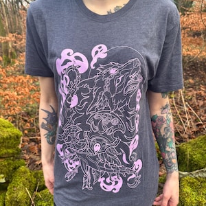 May include: A dark heather grey t-shirt featuring a pink graphic print of a wolf howling at the moon. The wolf is surrounded by swirling smoke and floral elements.