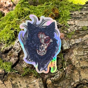 May include: A holographic sticker featuring a black wolf with a skull-like face and intricate details. The wolf is surrounded by a swirling, iridescent background.