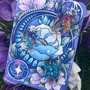 May include: A blue and purple card with a floral design and three clear glass dragon charms. The dragons are in different colours and have intricate details. The card is surrounded by a white border.