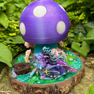 May include: A purple and white mushroom lamp with a fairy figurine sitting underneath. The mushroom is on a wooden base with a green and brown painted design.
