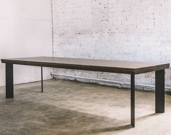 May include: A dark brown rectangular dining table with black metal legs. The table has a thick, textured wooden top and is supported by four black legs, two of which are wide and flat, and two are thin and round.