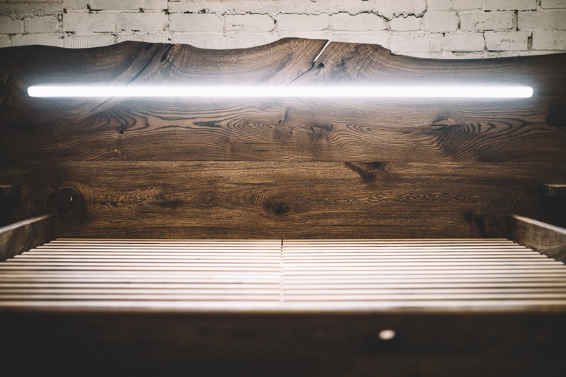 May include: A wooden bed frame with a headboard featuring a live edge design. The headboard is made of dark brown wood and has a built-in, horizontal LED light. The bed frame has a slatted base.