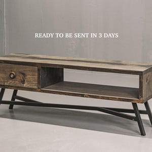 Peut inclure: Un meuble télé rectangulaire en bois avec une finition brun foncé, comprenant un tiroir avec un bouton circulaire et une étagère de rangement ouverte. L'unité est soutenue par un cadre en métal noir avec des pieds inclinés. Texte : READY TO BE SENT IN 3 DAYS.