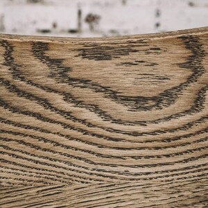 Puede incluir: Primer plano de una superficie de madera curvada con un patr&oacute;n de vetas naturales. La madera es de color marr&oacute;n claro con l&iacute;neas onduladas de color marr&oacute;n oscuro. La textura es visible, mostrando la veta natural.