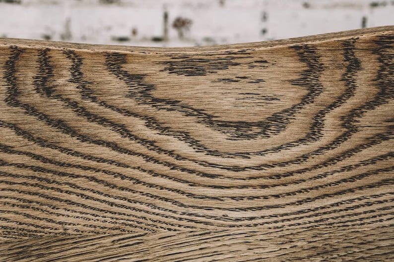 Puede incluir: Primer plano de una superficie de madera curvada con un patr&oacute;n de vetas naturales. La madera es de color marr&oacute;n claro con l&iacute;neas onduladas de color marr&oacute;n oscuro. La textura es visible, mostrando la veta natural.