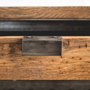 Puede incluir: Primer plano de una secci&oacute;n de mesa de madera con un soporte met&aacute;lico. La madera tiene una veta natural y un color marr&oacute;n c&aacute;lido. El soporte met&aacute;lico es rectangular y se fija con dos tornillos.