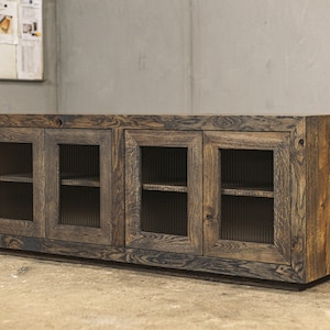 Puede incluir: Un aparador rústico de madera con cuatro puertas de cristal. El mueble es de madera teñida oscura con vetas visibles. Las puertas tienen un diseño de vidrio acanalado. El aparador es bajo y rectangular.