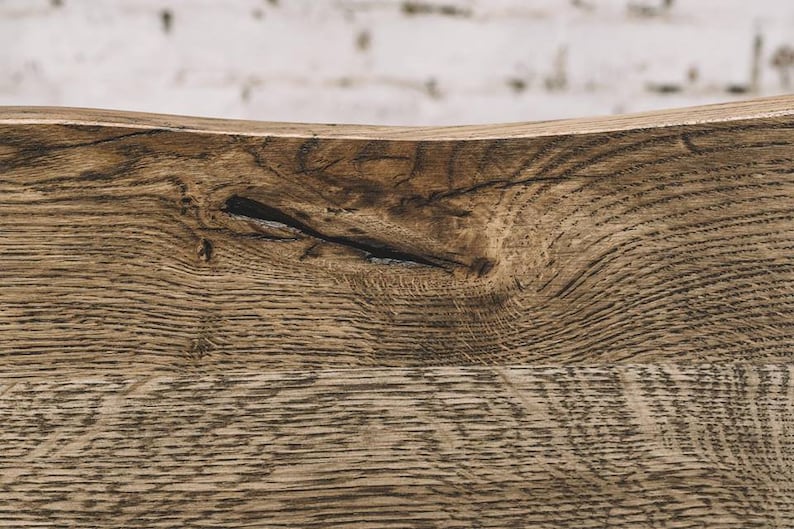 Puede incluir: Primer plano de una secci&oacute;n de madera envejecida, que muestra patrones de vetas naturales y un nudo. La madera tiene un tono marr&oacute;n c&aacute;lido con vetas m&aacute;s oscuras, lo que sugiere edad y textura. El fondo es una pared de ladrillos blancos borrosa.
