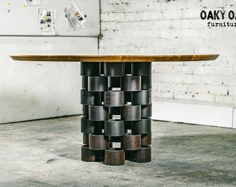 May include: A modern, round-top table with a wooden surface and a unique base made of stacked, dark metal rings. The table is a statement piece, perfect for a living room or dining area. The logo "Oaky Oak furniture" is visible in the top right corner.