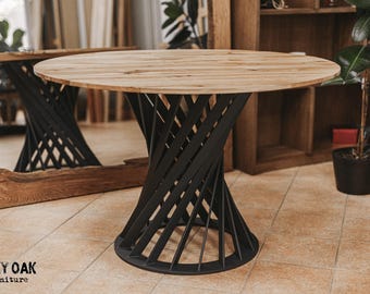 May include: Round wooden table with a light-colored top and a black, geometric base. The base has a spiral design. The table is in a room with a tiled floor and wooden furniture. The table is approximately 36 inches in diameter.