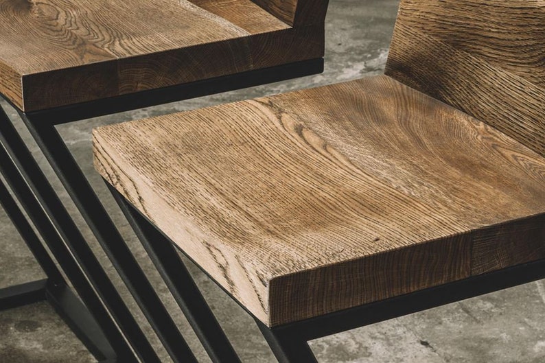 Puede incluir: Primer plano de dos sillas de madera con acabado de vetas naturales. Los asientos son rectangulares y est&aacute;n soportados por una estructura met&aacute;lica negra con un dise&ntilde;o geom&eacute;trico. Las sillas tienen una est&eacute;tica moderna y minimalista.