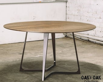 May include: A round wooden table with a light brown tabletop and a metal base. The table has a diameter of approximately 48 inches. The base is made of dark gray metal legs that connect to a central support structure.