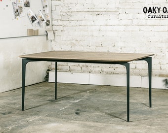 May include: A rectangular wooden table with a light brown surface and black metal legs. The table is in a room with a white brick wall and the text "Oaky Oak furniture" is visible in the upper right corner.