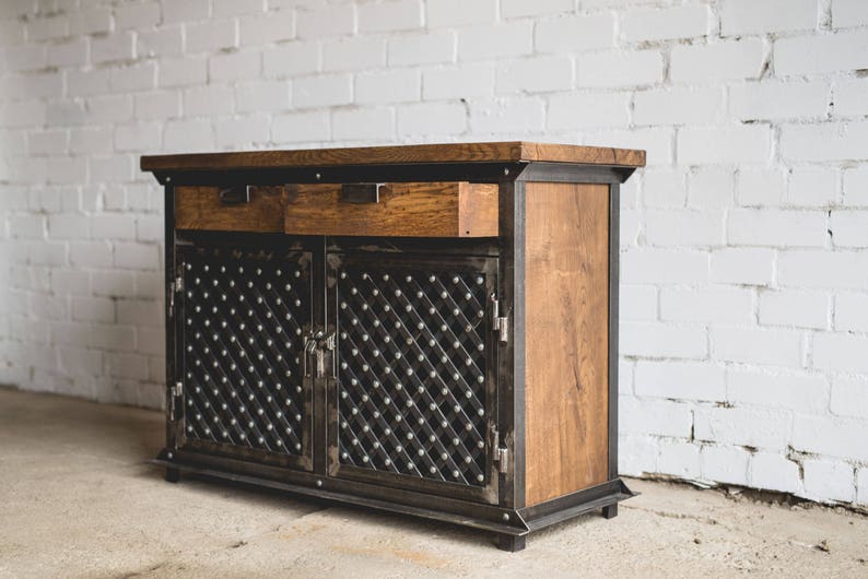 Puede incluir: Un mueble de madera con marco y detalles de metal oscuro. El mueble tiene dos cajones y dos puertas con un patr&oacute;n de diamantes. La madera es de color marr&oacute;n c&aacute;lido y el metal es gris oscuro. Es un mueble.