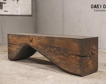 Puede incluir: Un banco de madera marrón oscuro con un diseño curvo único. El banco está hecho de una sola pieza de madera gruesa, mostrando la veta y textura natural. El logotipo de OAKY OAK furniture está en la esquina superior derecha.