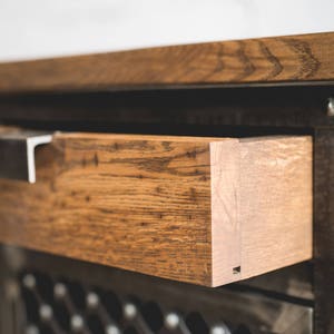 Puede incluir: Primer plano de un mueble de madera con un caj&oacute;n abierto. El caj&oacute;n es de madera marr&oacute;n claro con vetas visibles y est&aacute; acentuado con un tirador de metal. El mueble tiene un marco de metal oscuro y un frente decorativo.