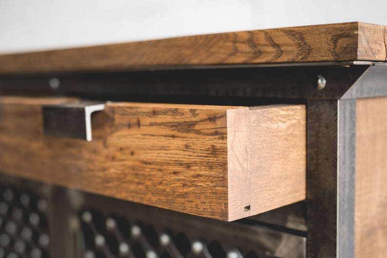Puede incluir: Primer plano de un mueble de madera con un caj&oacute;n abierto. El caj&oacute;n es de madera marr&oacute;n claro con vetas visibles y est&aacute; acentuado con un tirador de metal. El mueble tiene un marco de metal oscuro y un frente decorativo.