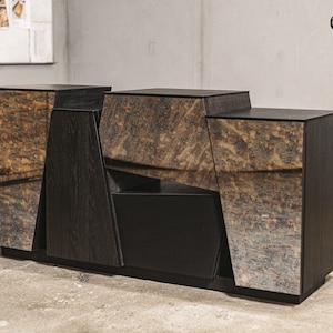 Puede incluir: Un mueble de madera moderno y geométrico con un acabado oscuro y paneles texturizados y espejados. El mueble presenta un diseño angular único con una base negra y el texto "Oaky Oak furniture".