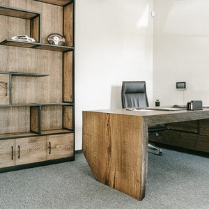Puede incluir: Un espacio de oficina moderno con un gran escritorio de madera con un diseño de borde vivo y una estantería a juego. El escritorio tiene cajones y una silla de cuero negro. La estantería tiene estantes abiertos y armarios.