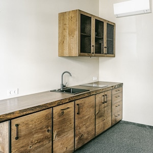 Puede incluir: Una moderna cocina con gabinetes y encimeras de madera. Los gabinetes tienen manijas negras y un fregadero y una placa de cocina integrados. Los gabinetes superiores tienen puertas de vidrio con un diseño de malla. La pared es blanca y el suelo es gris.