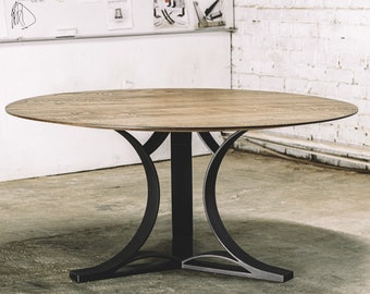 May include: A round wooden dining table with a light brown finish. The table has a black metal base with curved supports. The table is approximately 48 inches in diameter and is suitable for a dining room or kitchen.
