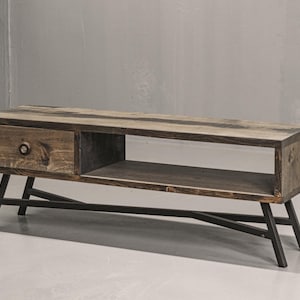 May include: A rectangular media console constructed from dark stained wood featuring a single drawer on the left side with a circular knob and an open storage shelf on the right. The unit is supported by a black metal frame with angled legs.
