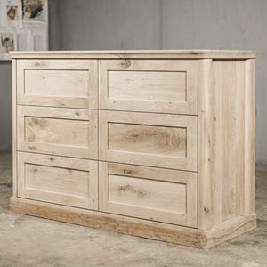 Puede incluir: Una cómoda de madera clara con seis cajones. La cómoda tiene forma rectangular con una base ligeramente curvada y una parte superior plana. La veta de la madera es visible y la pieza tiene un acabado natural. El logotipo "Oaky Oak Furniture" está en la esquina superior derecha.