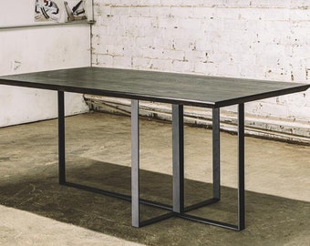 May include: A rectangular dark wood table with a black metal frame. The table is approximately 72 inches long and 36 inches wide. The legs are a geometric design, providing a modern aesthetic. The table is set against a white brick wall.