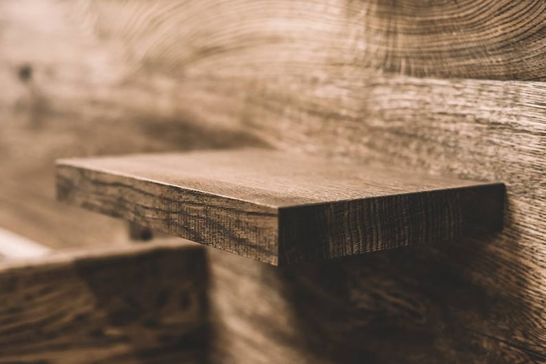 May include: Close-up of a floating wooden shelf with a dark brown finish. The shelf is rectangular and appears to be made of solid wood, with visible grain and texture. The background is a wooden wall.