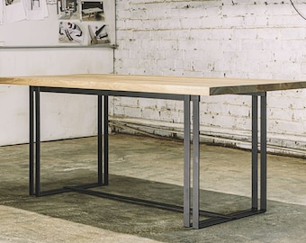 May include: A rectangular wooden table with a light-colored top and a dark gray metal frame. The table has a simple, modern design, suitable for a dining or work space. The legs are made of rectangular metal bars.