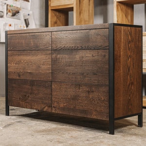 Puede incluir: Una cómoda de madera marrón oscuro con seis cajones y un marco de metal negro. La cómoda tiene un acabado de vetas de madera natural y está sobre un fondo neutro. El logotipo de OAKY OAK furniture está en la esquina superior izquierda.